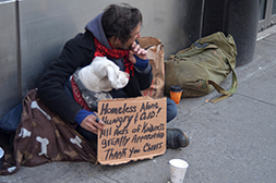 Homeless man and dog sitting with a sign on the sidewalk